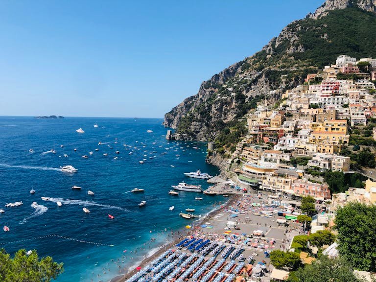 Scenic view of Amalfi Coast settlement located on green cliff near picturesque blue sea with floating boats on sunny summer day