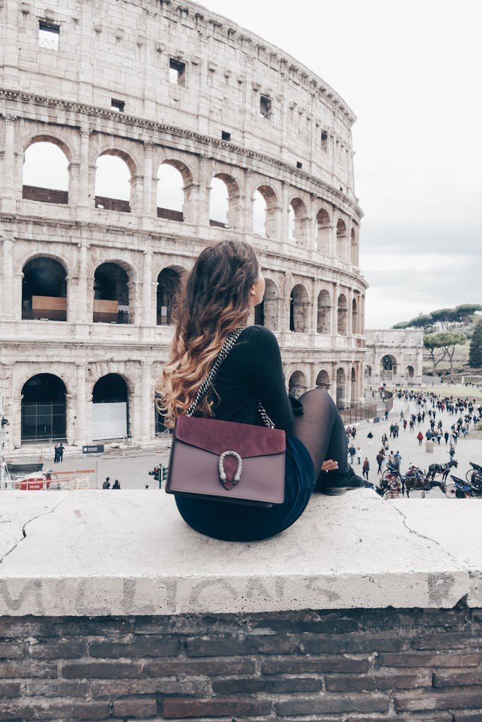 Woman with stylish bag resting on stone wall near Colosseum